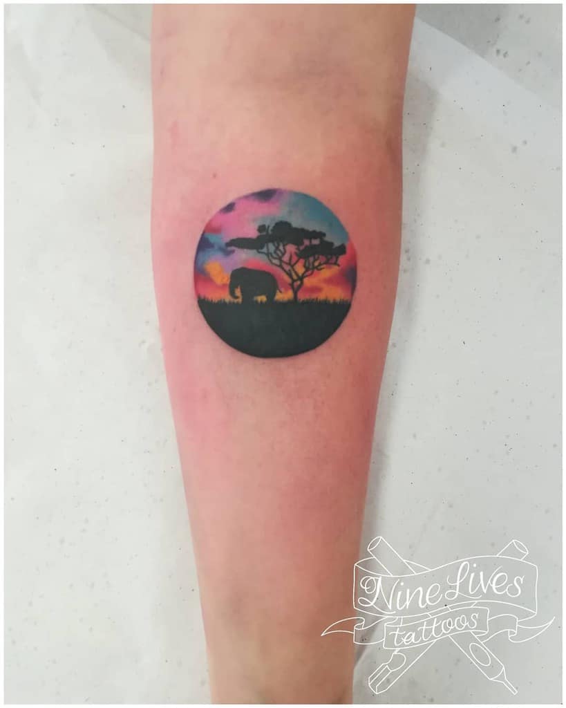Tattoo of a sunset scene with an elephant and tree on an arm