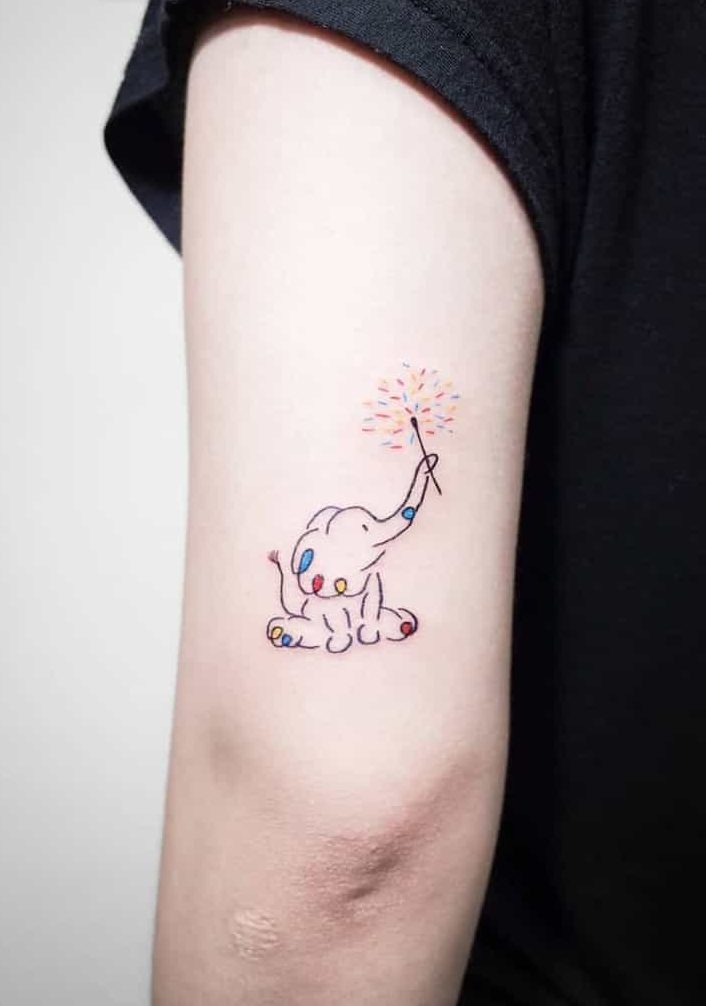 Small, colorful elephant tattoo on an arm, with its trunk raised and holding a sparkler