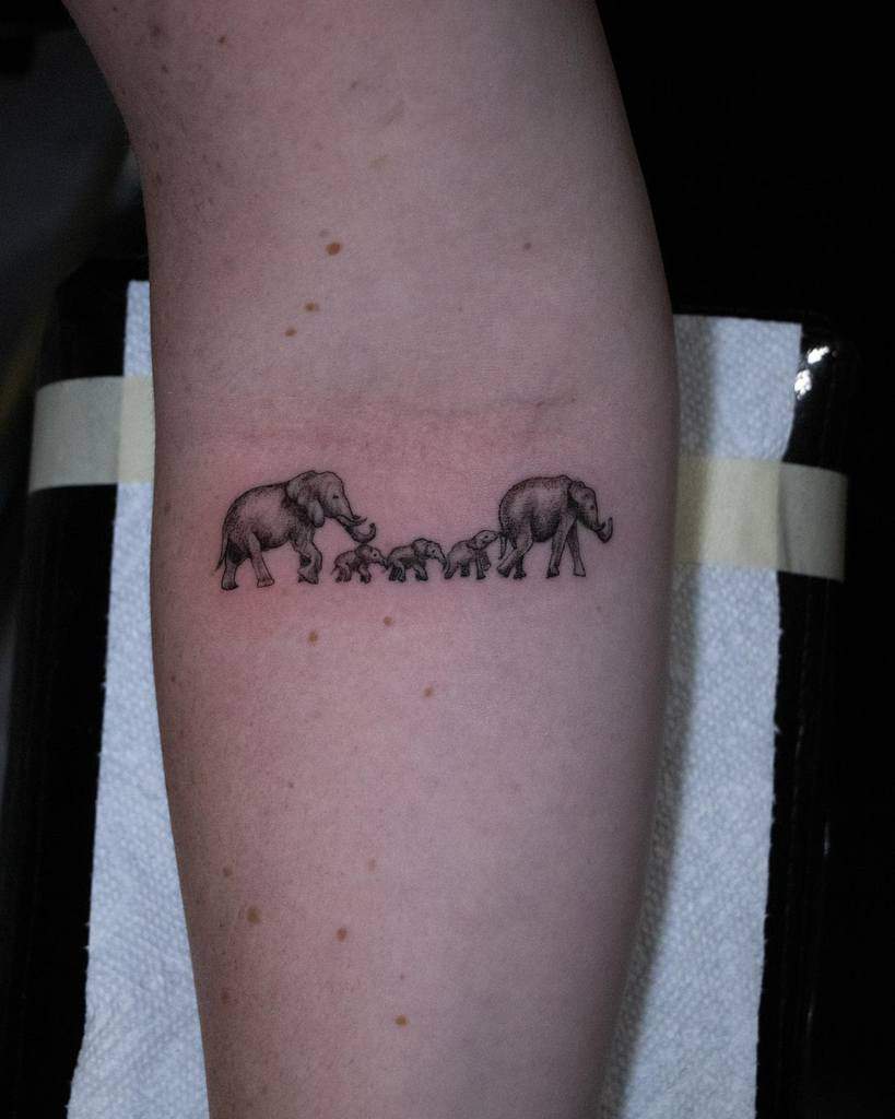 Tattoo of two adult elephants and three baby elephants walking in a line on a forearm