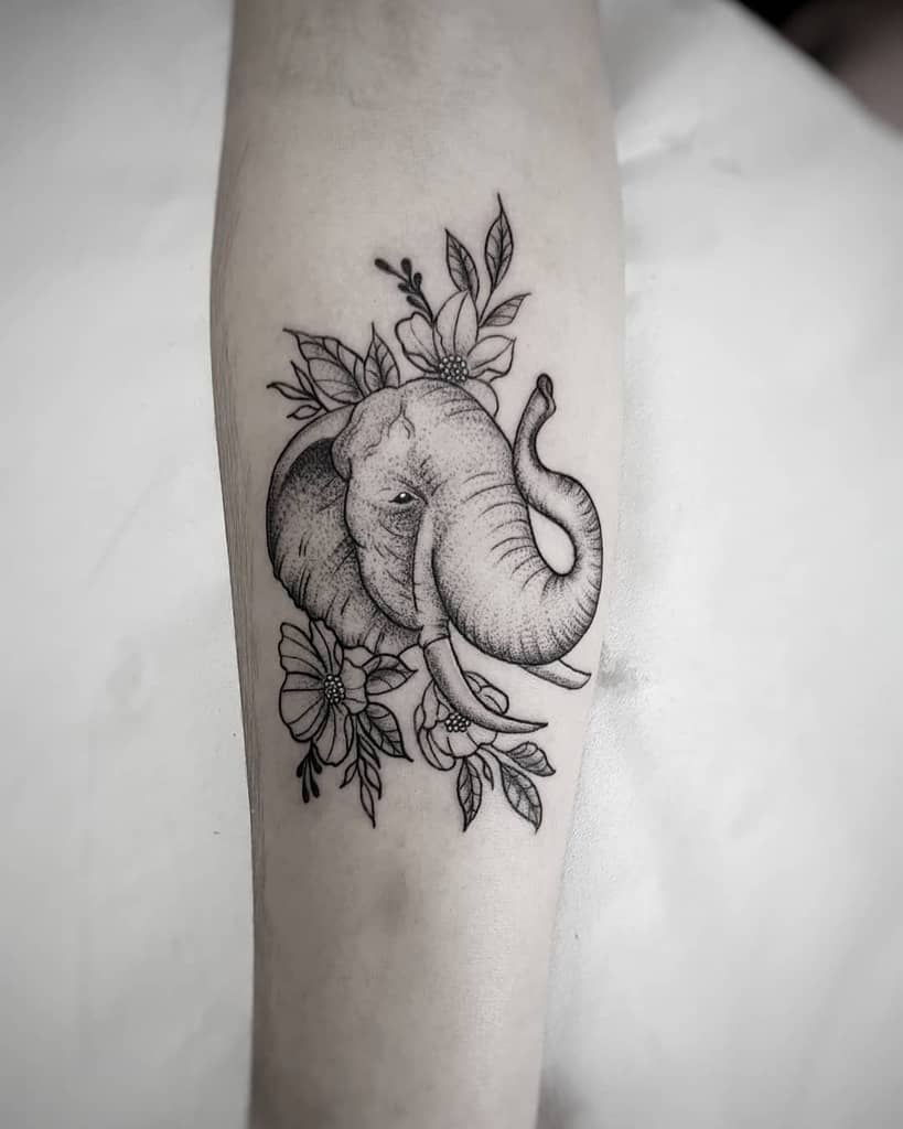 Black and grey elephant tattoo with floral accents on a forearm
