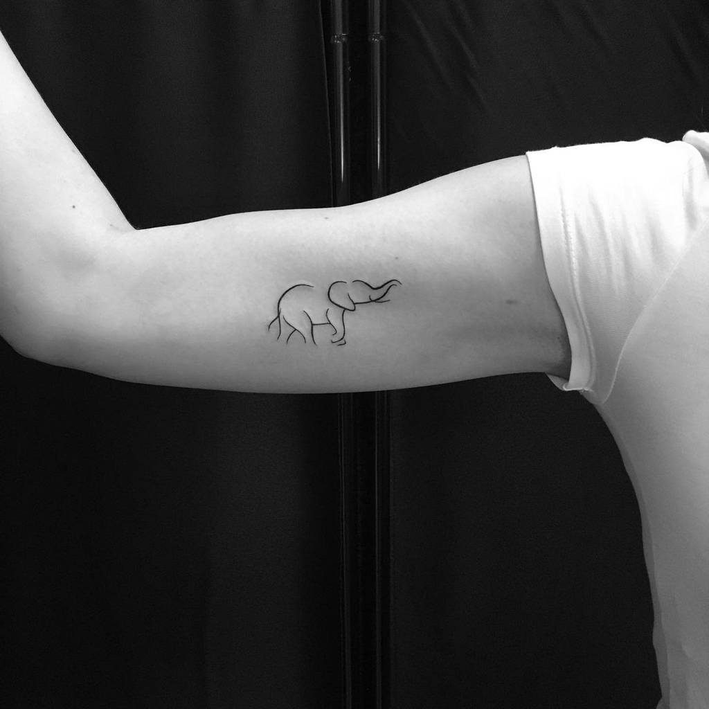 Minimalist elephant outline tattoo on the upper arm, featuring a sleek and elegant line art design