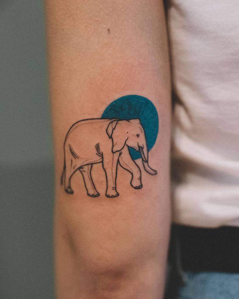 Tattoo of a walking elephant with a blue circle in the background on an arm