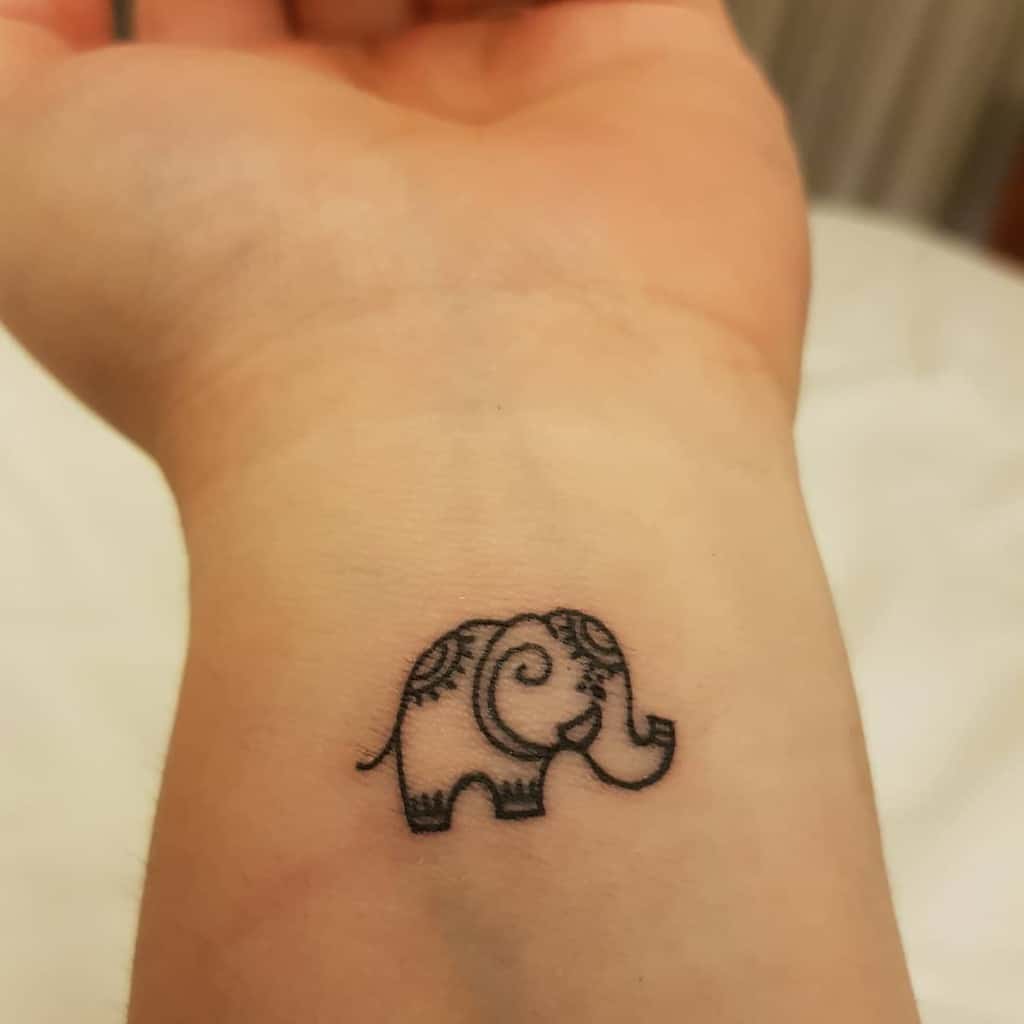 A small, intricate elephant tattoo on a person's wrist with a decorative pattern on its back