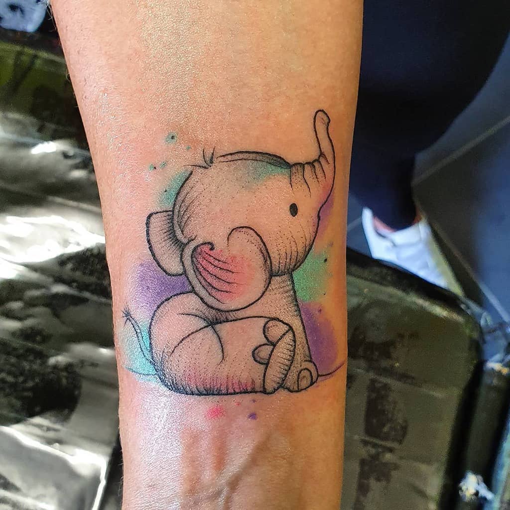 Tattoo of a cute baby elephant with colorful watercolor splashes on an arm