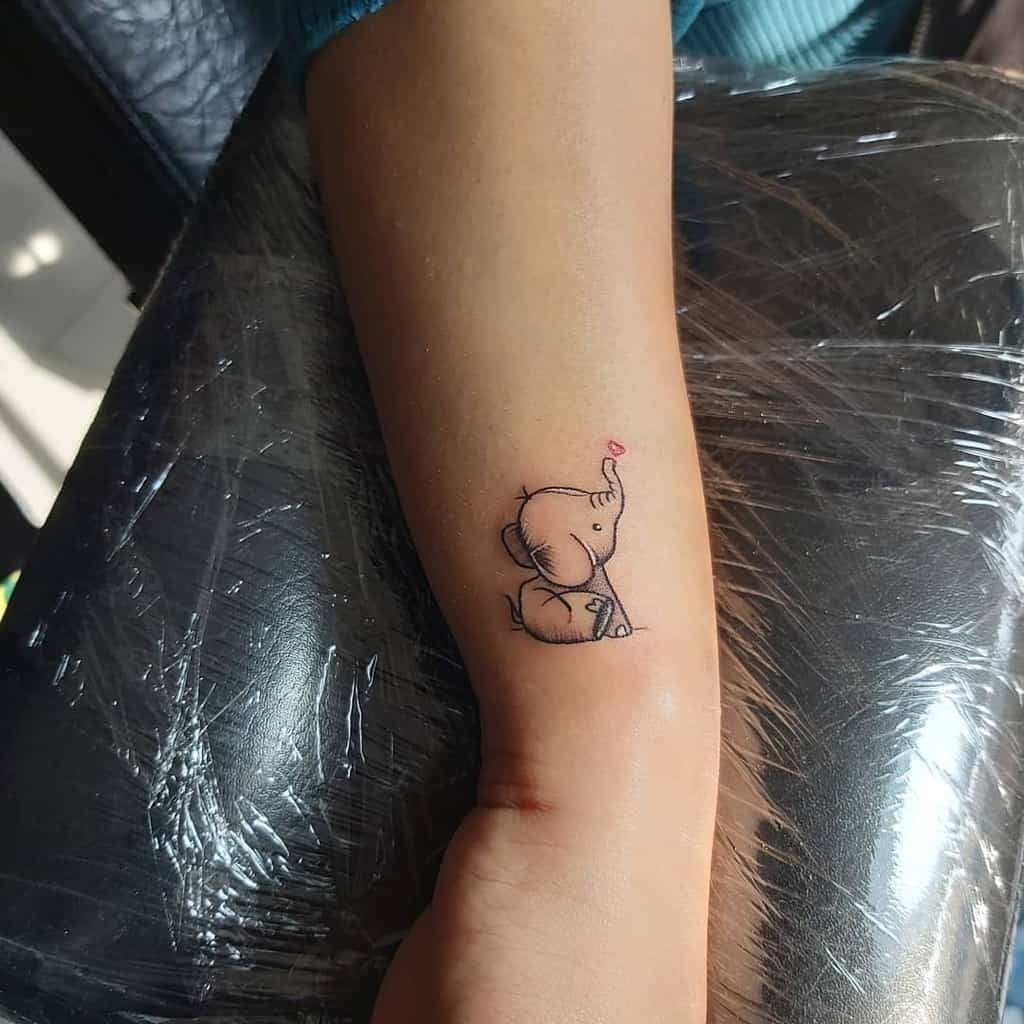 A small tattoo of a cute elephant sitting with its trunk raised on a forearm