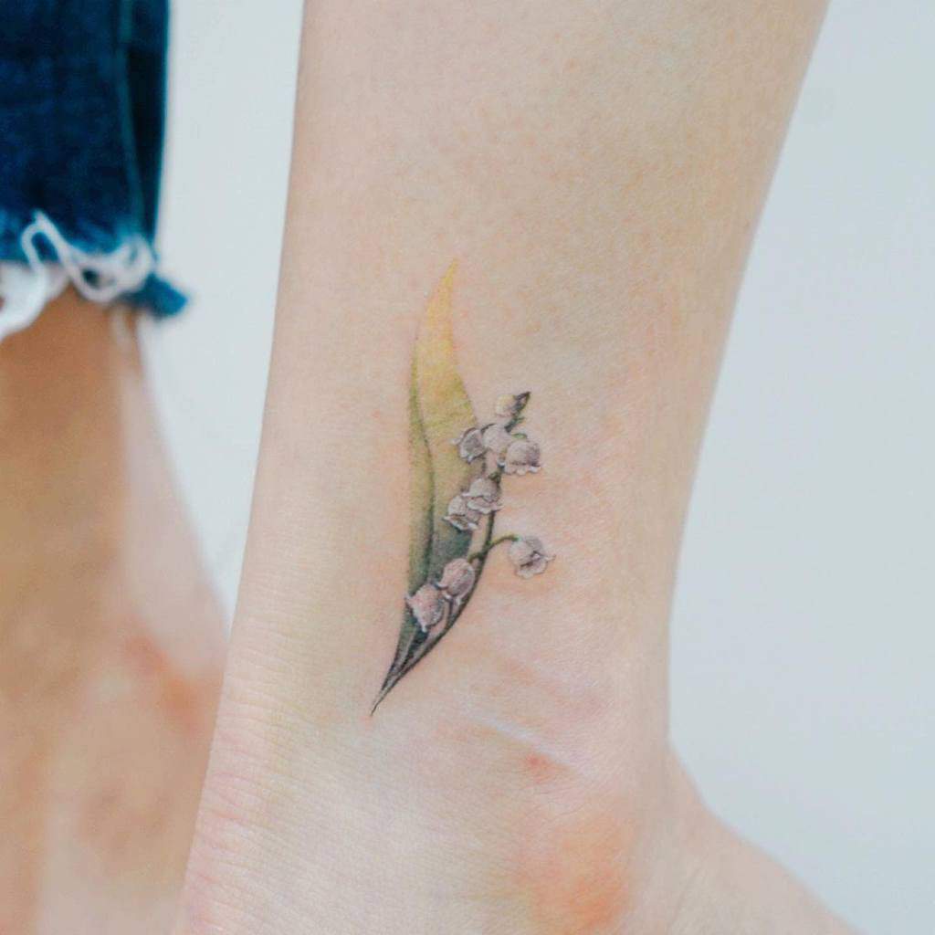 Ankle tattoo of a delicate flower with small white blooms and a green leaf