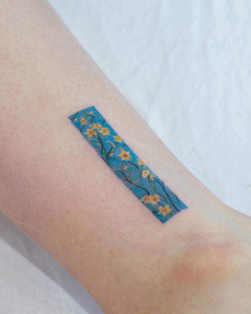 Tattoo on arm: a slim blue rectangle with delicate yellow flowers and green branches