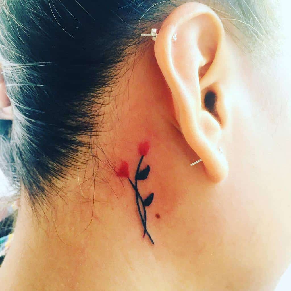 A delicate flower tattoo with black stem and red petals is behind an ear
