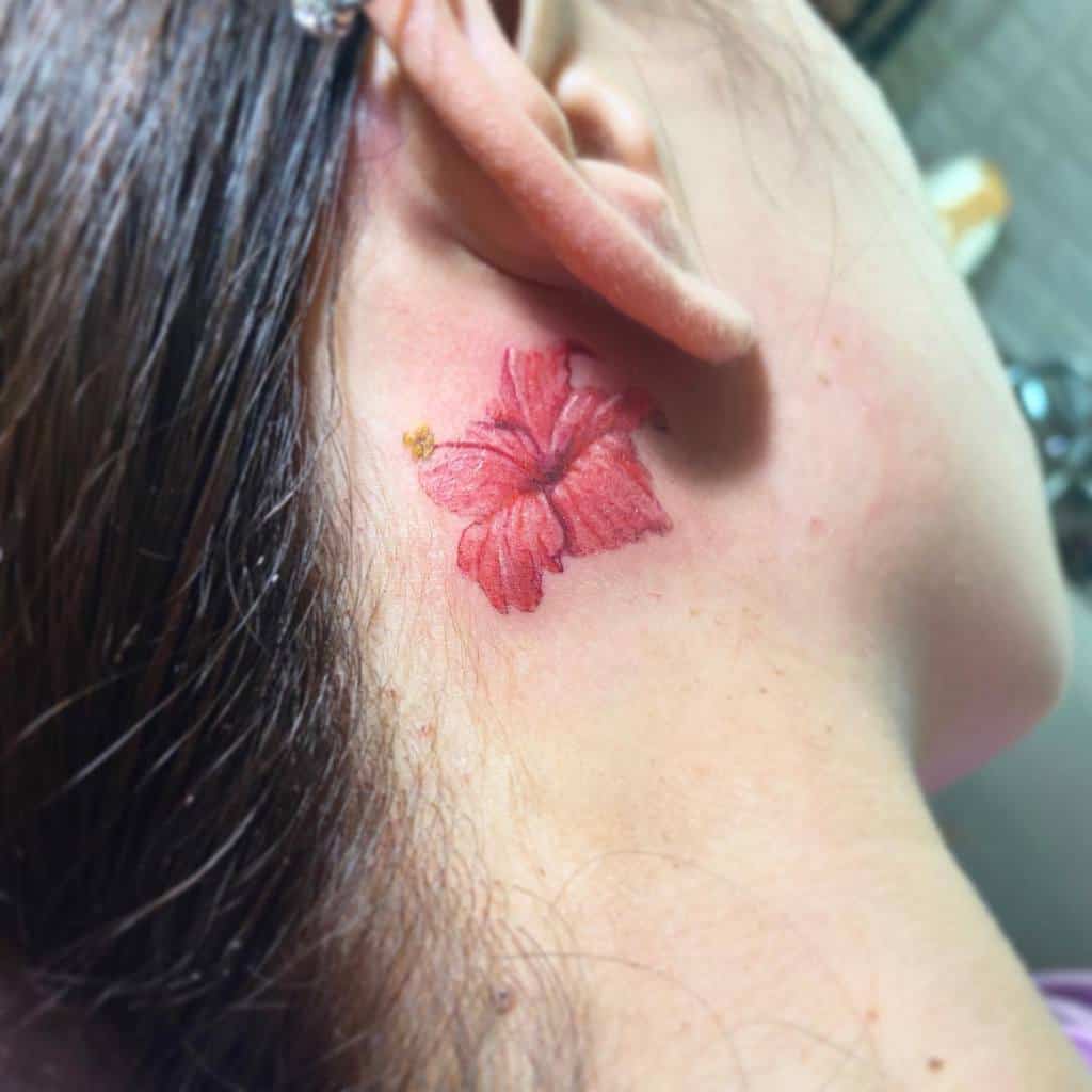 A red hibiscus tattoo is located behind an ear