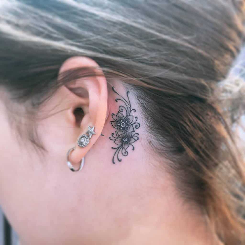 Behind-the-ear tattoo featuring intricate floral designs with delicate details in black ink