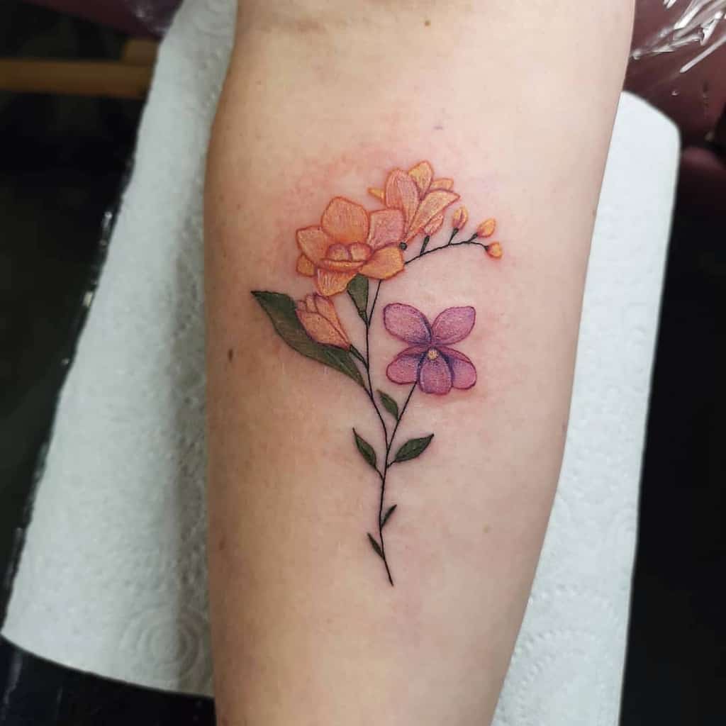 Tattoo of an orange flower with green leaves and a purple flower on a forearm