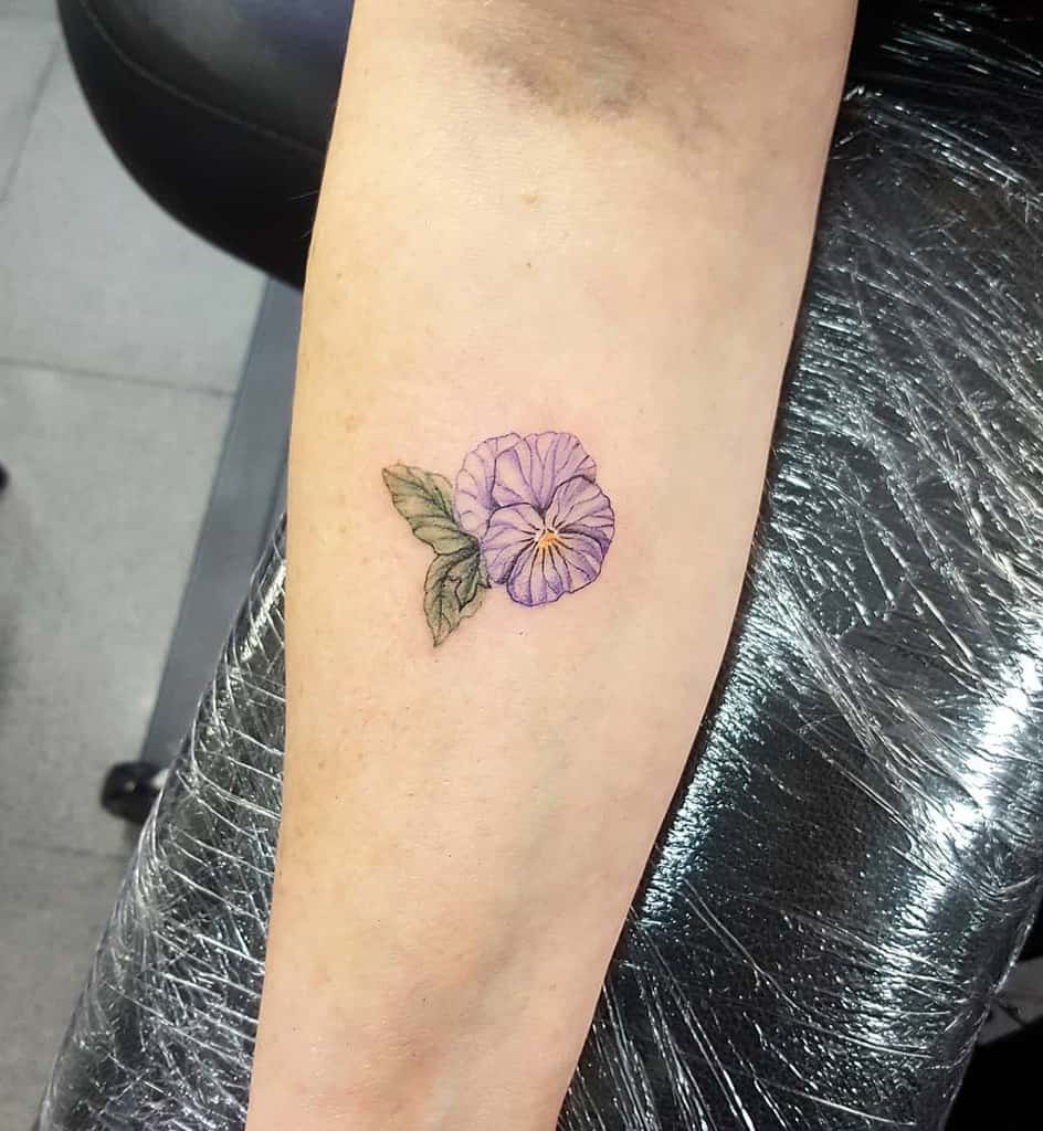 Tattoo of a purple flower with green leaves on a forearm