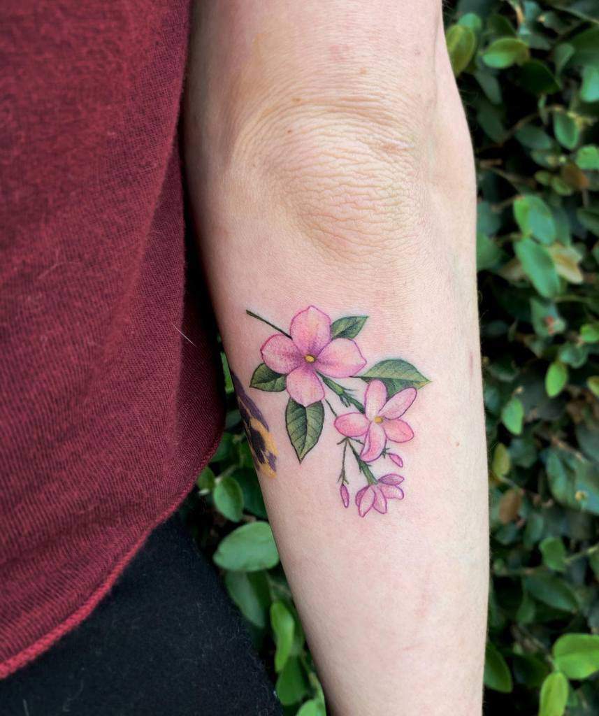 Flower tattoo with pink blooms and green leaves on an arm