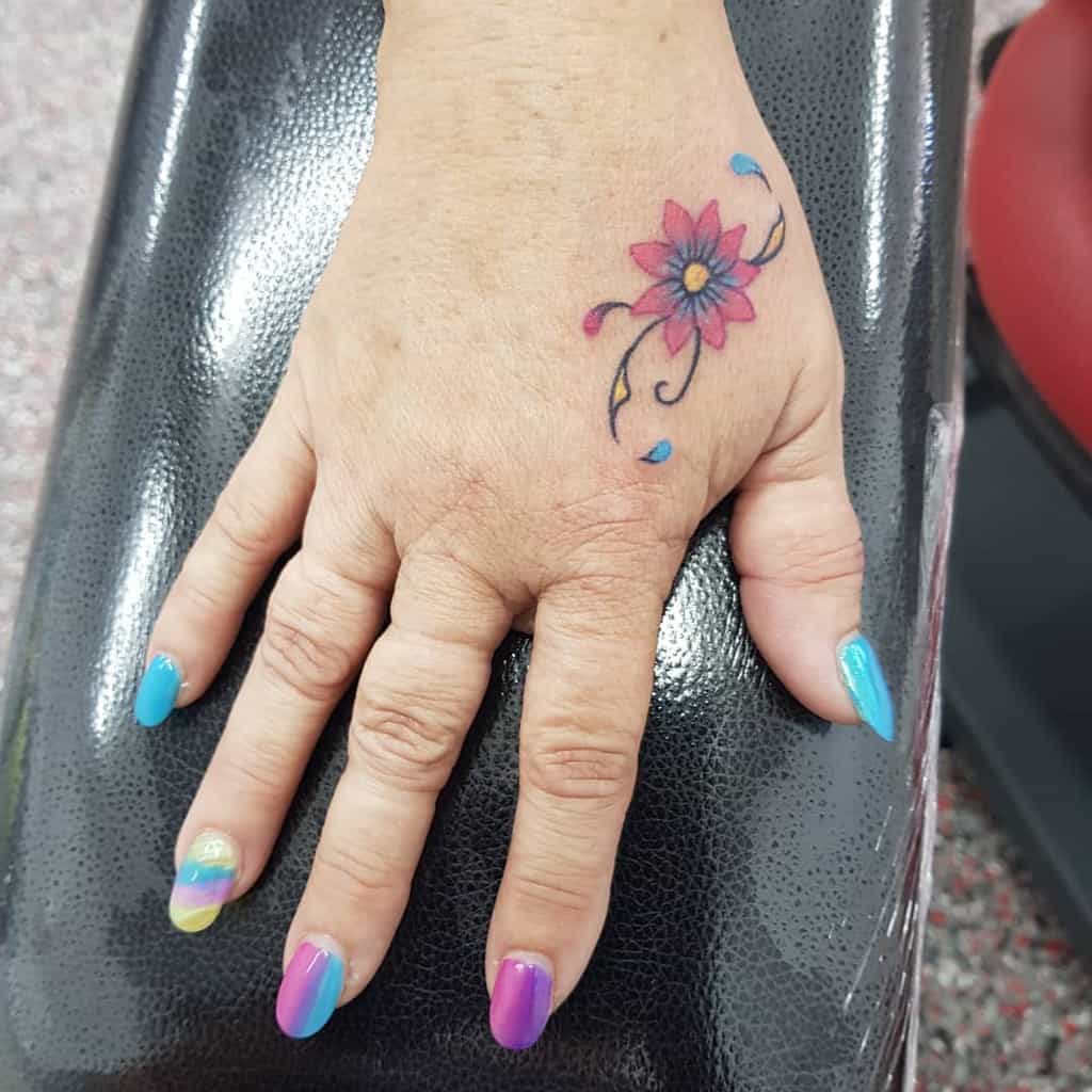 Colorful hand tattoo of a pink and purple flower with delicate swirls and blue petal-like accents