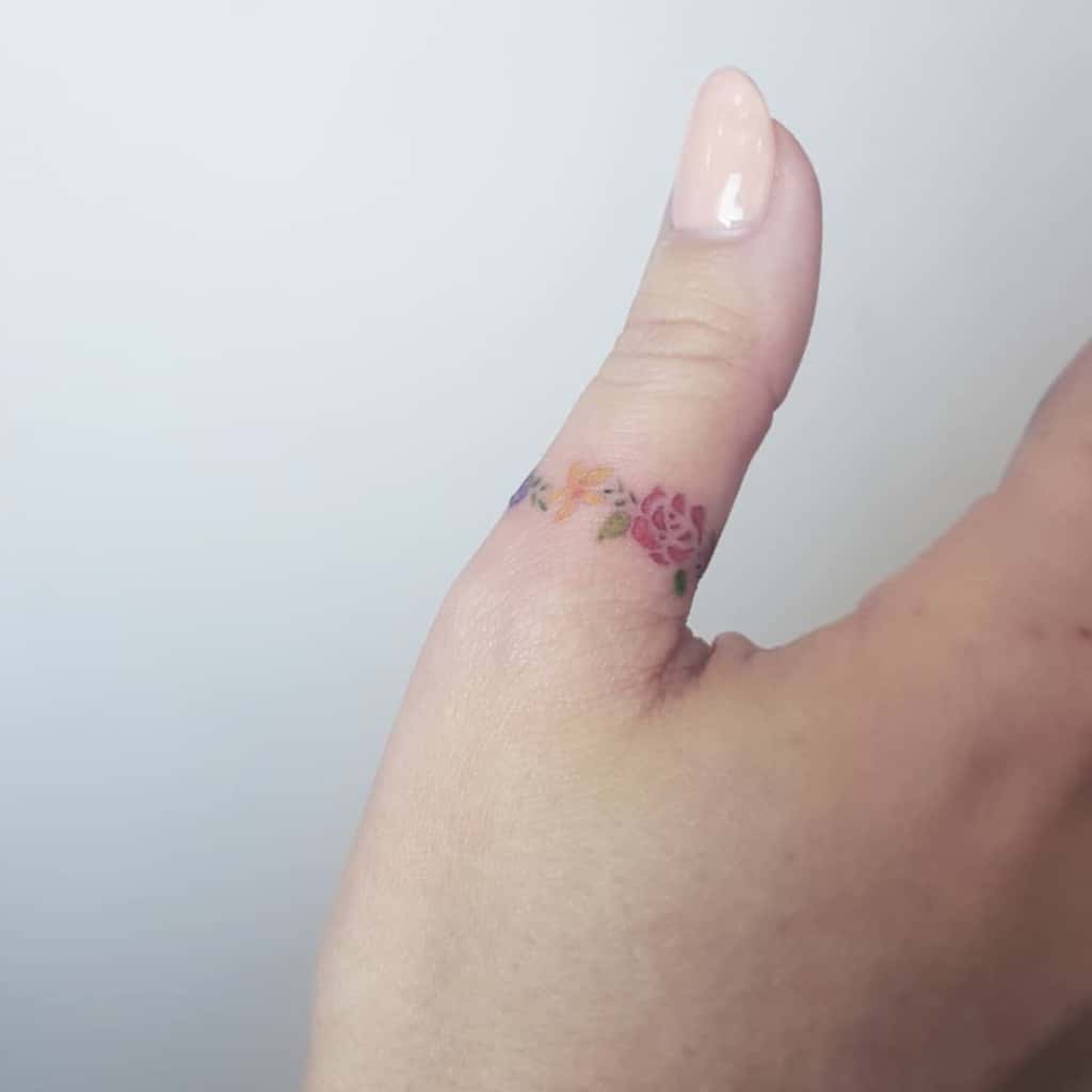 Thumb with a delicate floral tattoo featuring roses and small flowers on the side