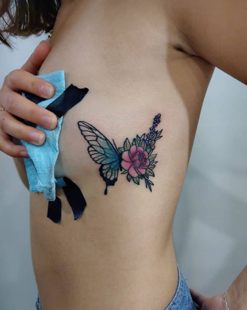 Colorful rib tattoo of a butterfly wing paired with vibrant flowers, including a pink rose and lavender sprigs