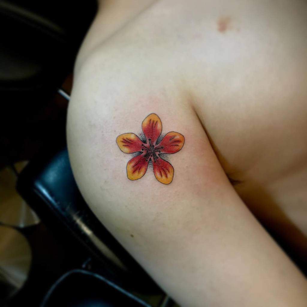 A vibrant flower tattoo on a person's upper arm, showcasing shades of red, orange, and yellow