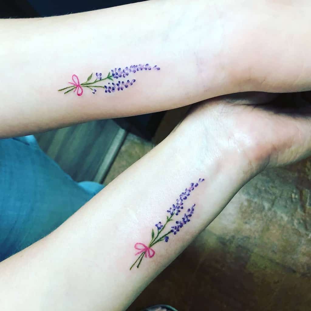 Two forearms with matching lavender sprig tattoos wrapped with pink bows