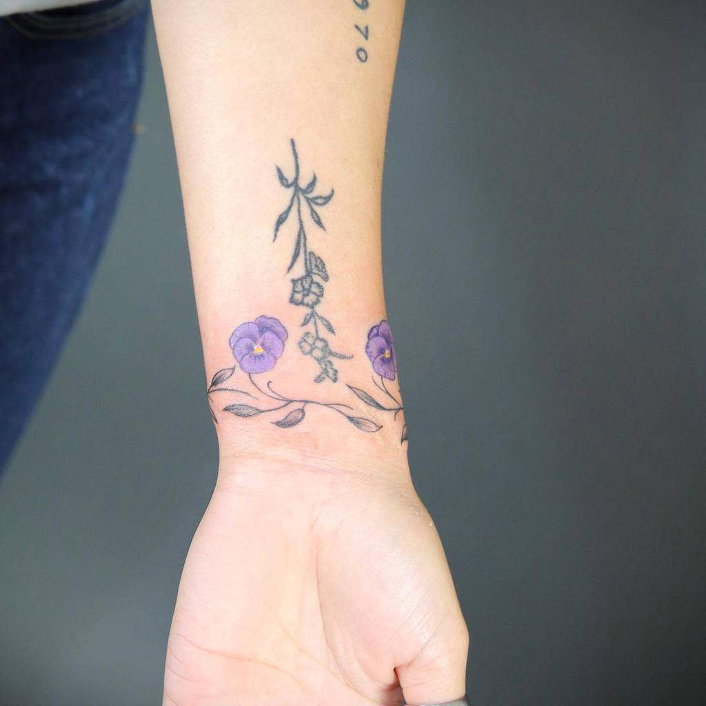 Wrist tattoo of purple flowers with green stems and leaves