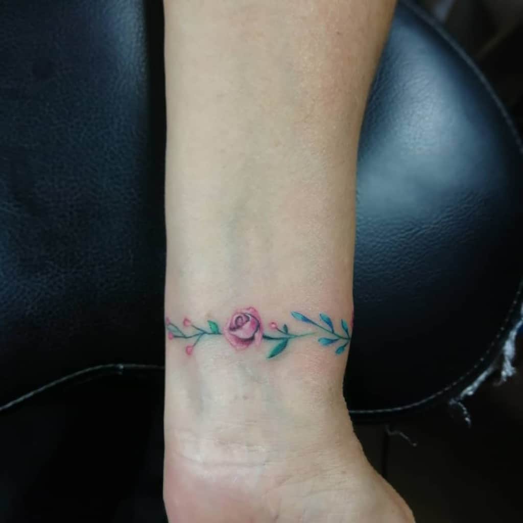 A delicate rose tattoo with leaves adorns a wrist