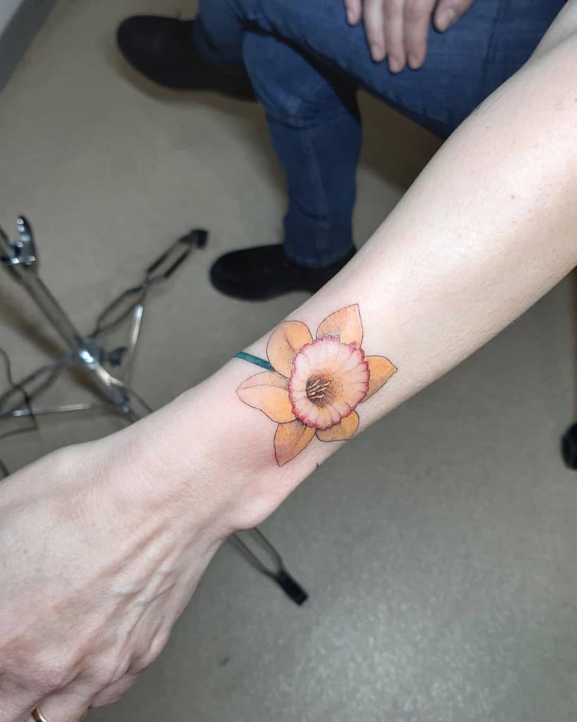 A vibrant orange daffodil tattoo on a wrist