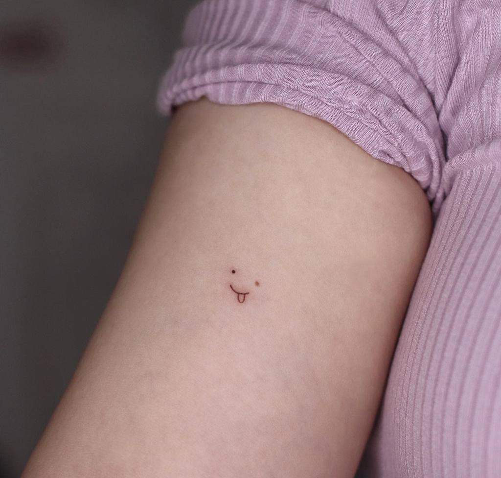 A small, simple smiley face tattoo with a tongue sticking out on a forearm