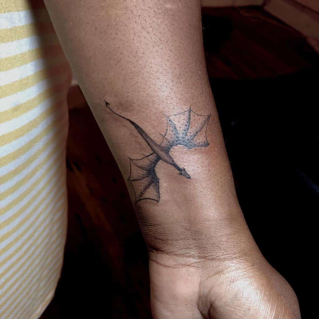 A small black dragon tattoo on a person's forearm