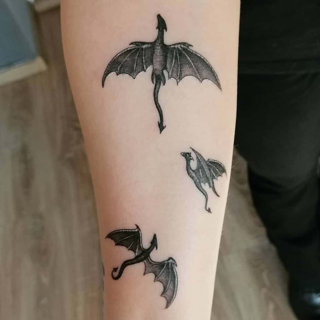 Three black dragon tattoos flying upwards on a person's forearm