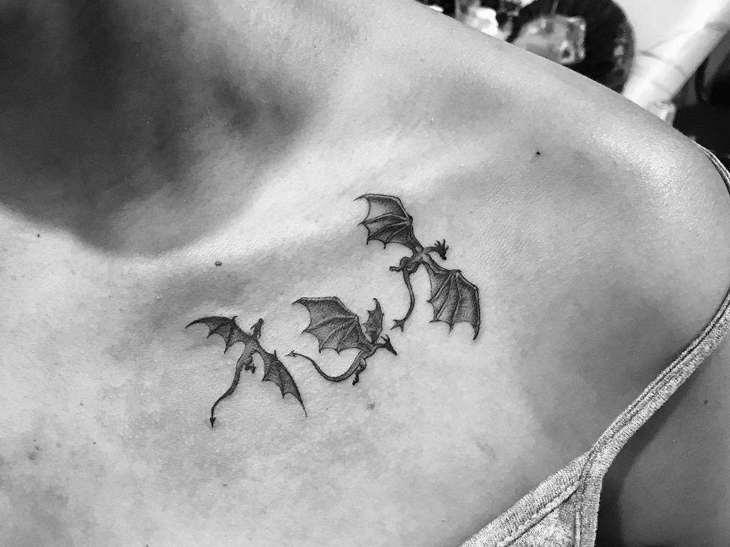 Black and white tattoo of three flying dragons on a person's shoulder