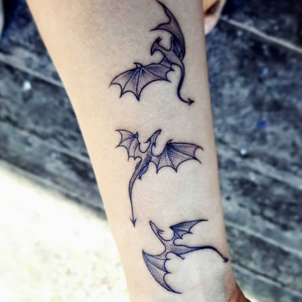 Three small dragon tattoos inked on a forearm in a descending line