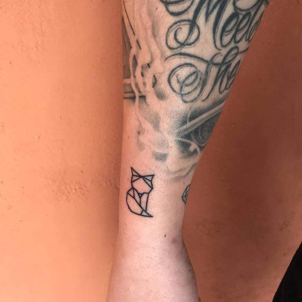 Geometric fox tattoo on a forearm with other tattoos visible in the background
