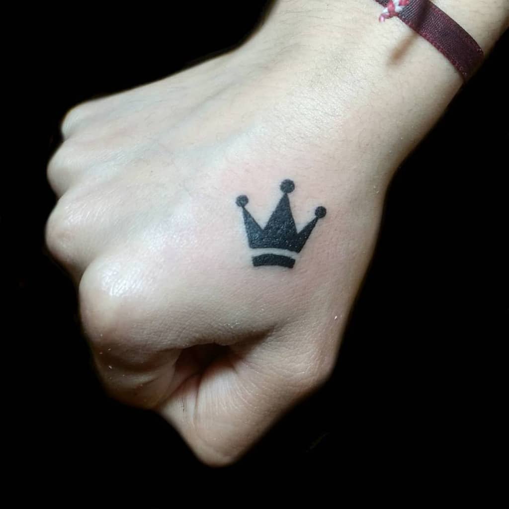 A hand with a small black crown tattoo on the back