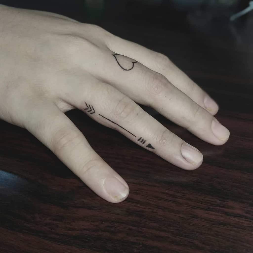 Hand with heart and arrow tattoos on fingers and knuckles