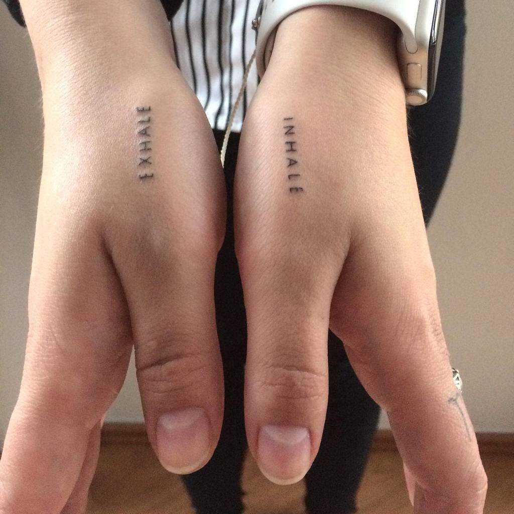 Hands with tattoos reading "EXHALE" and "INHALE" on the sides of the pinkie fingers
