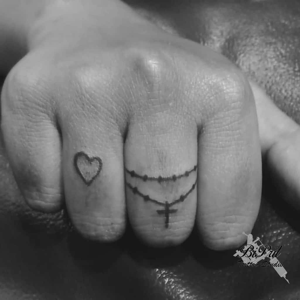 Close-up of a hand with ring finger tattoos of a heart and a rosary with a cross