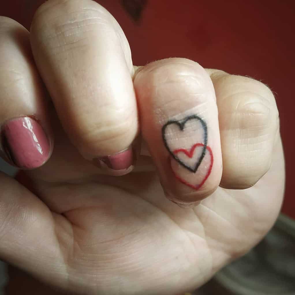 Fingers with pink nail polish and a double heart tattoo on the pinky knuckle
