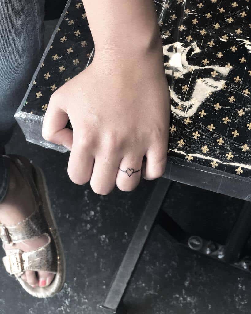 Hand with a heart-shaped ring tattoo on the finger, resting on a star-patterned surface