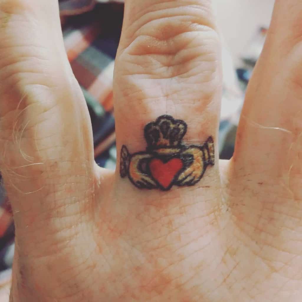 A Claddagh ring tattoo on a finger, featuring a heart, crown, and hands design