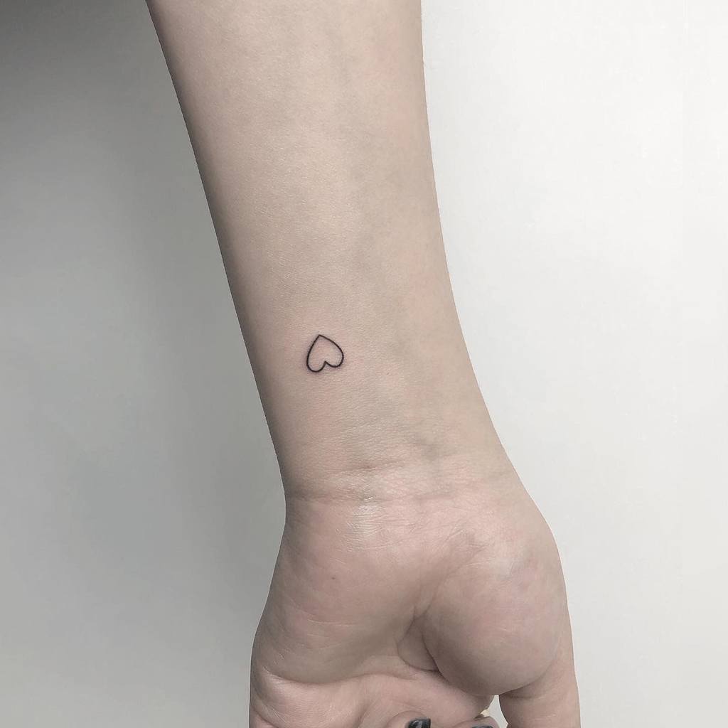 A small, simple heart outline tattoo on the inside of a person's wrist