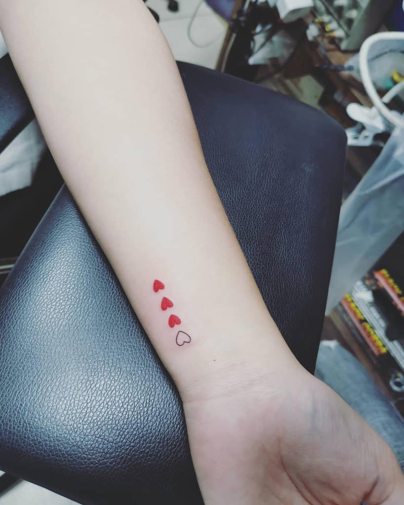 Wrist tattoo featuring a series of small red hearts gradually transitioning to a minimalist heart outline