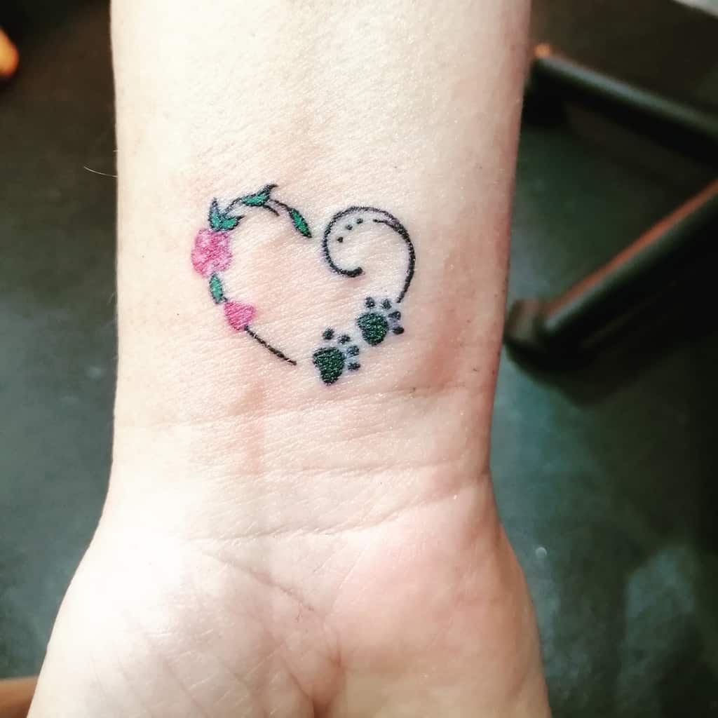Minimalist tattoo of a heart with floral elements and paw prints on a wrist