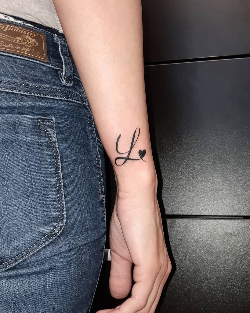 Close-up of a forearm tattoo featuring the letter "L" with a small heart