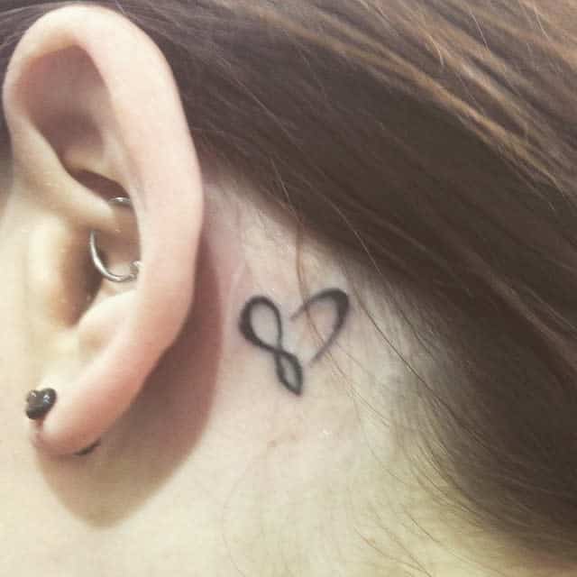 Small tattoo of a heart-shaped infinity symbol behind a person's right ear