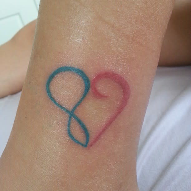 A tattoo of a heart shape blending blue and pink colors on a person's skin, intertwined with an infinity symbol