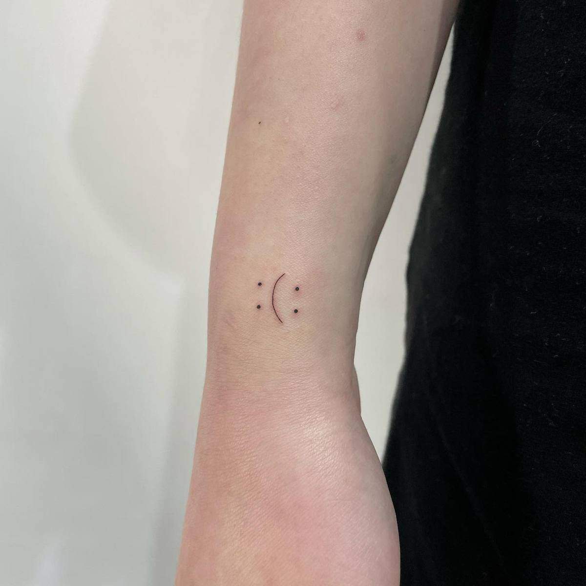 Small smiley or sad face tattoo on an arm