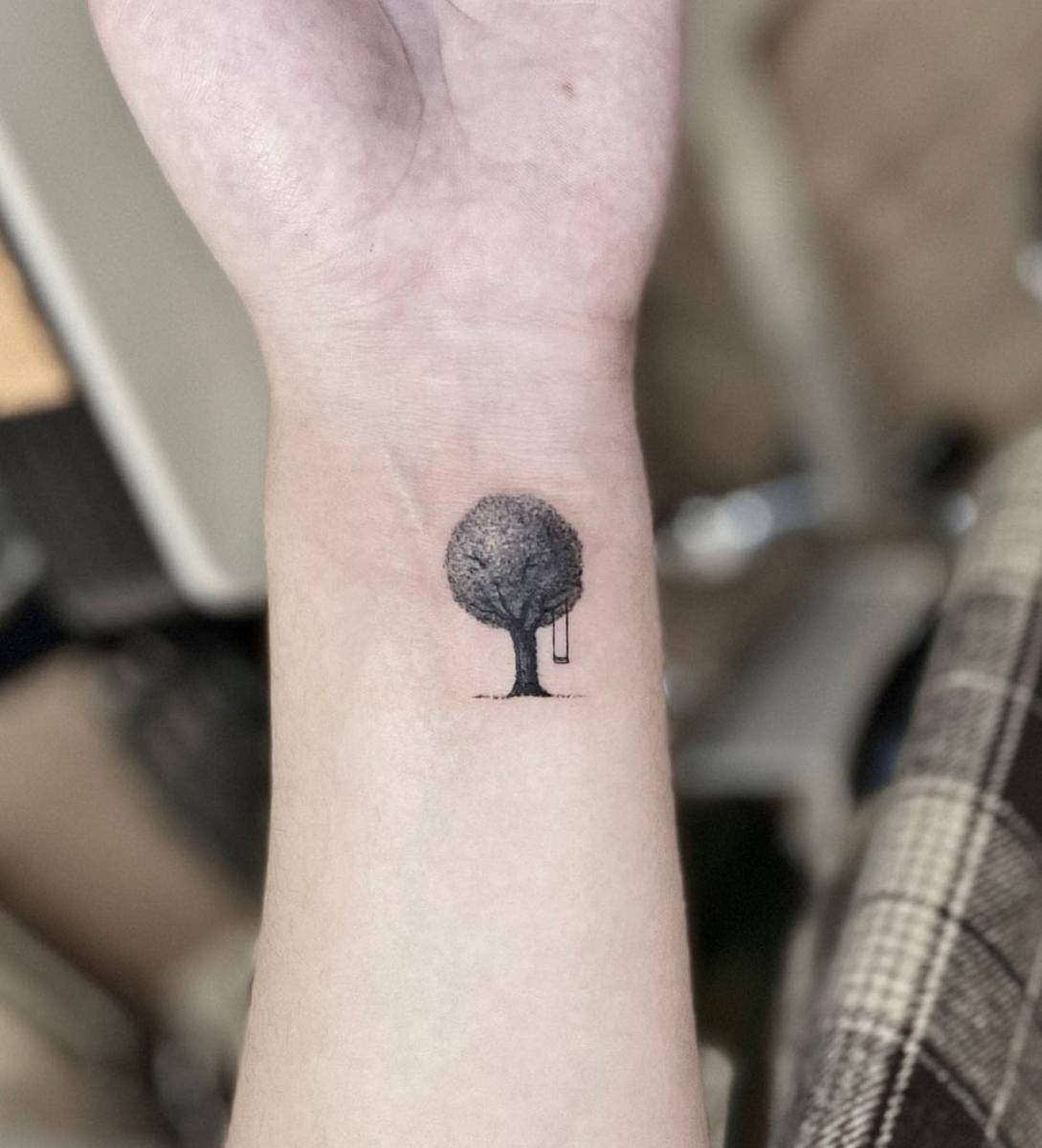 A small tree tattoo with a swing on a wrist