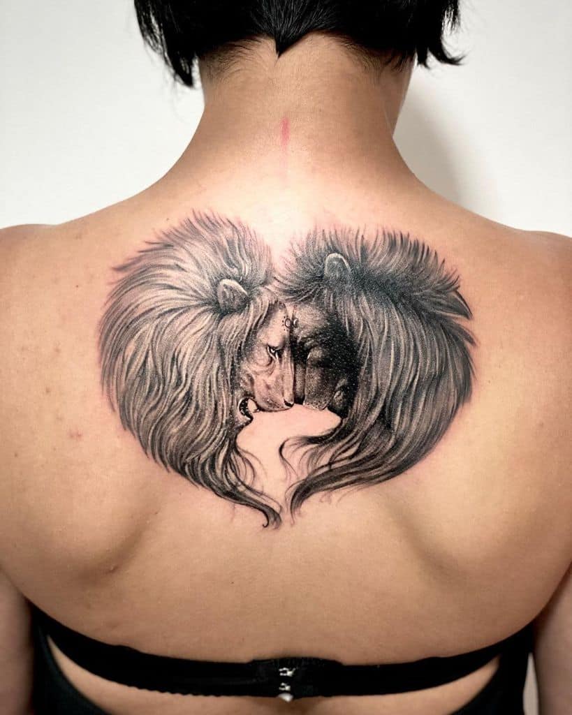 A detailed black and gray tattoo of two lions facing each other, forming a heart shape on the back