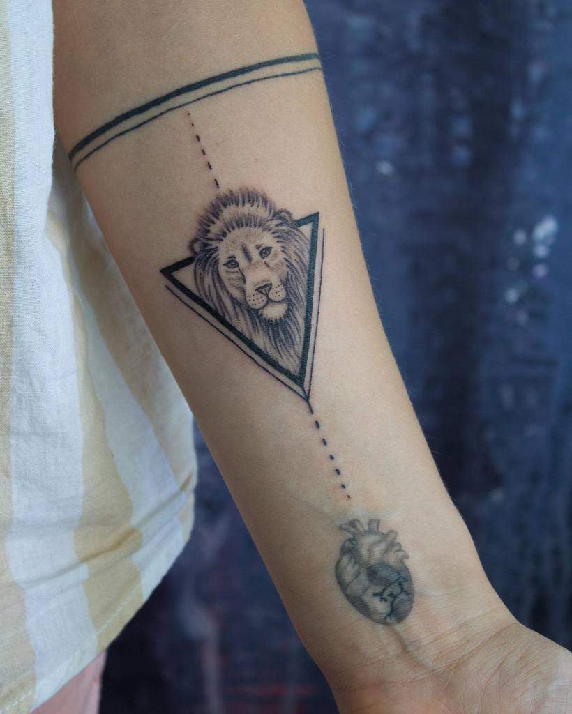 A small geometric tattoo featuring a lion's head inside a triangle, connected by a dotted line to a heart on the forearm