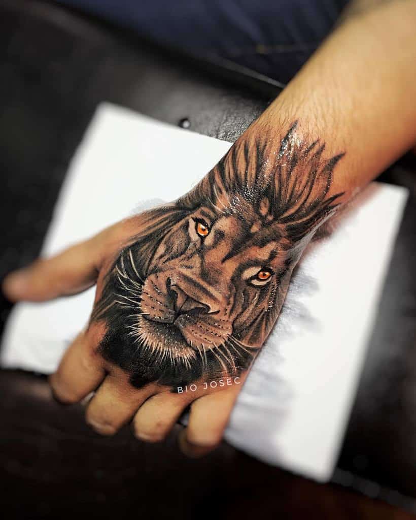 A hand adorned with an intricately detailed lion tattoo lies on the back, showcasing a majestic lion’s grace
