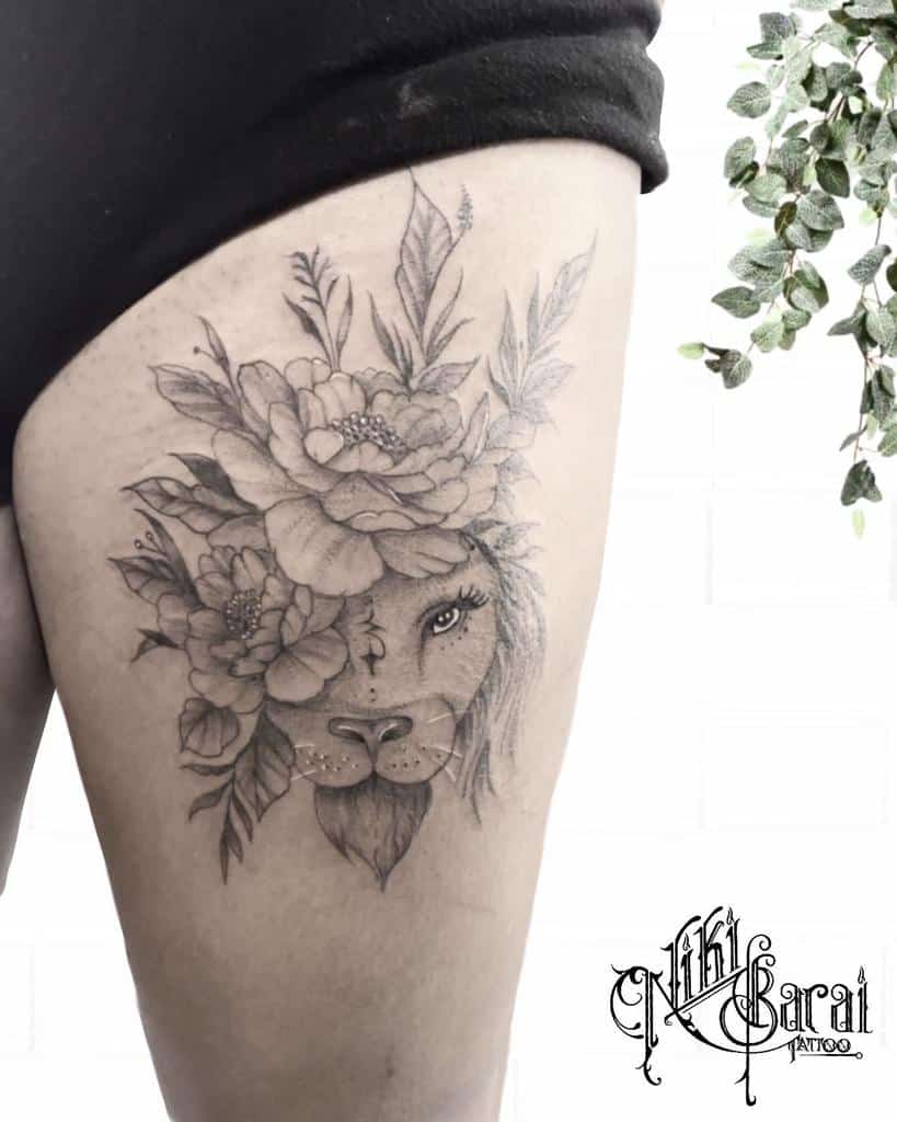 Thigh tattoo featuring a majestic lion with a vibrant floral mane and leafy accents